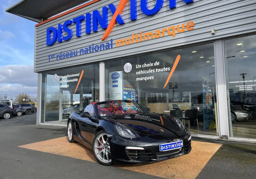 Porsche Boxster S noir intense vue 3/4 avant droit, capote ouverte et intérieur cuir rouge grenat visible.