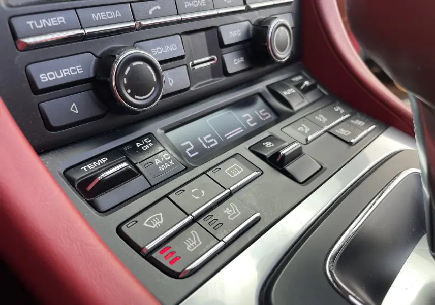 Gros plan sur la console centrale rouge grenat de la Porsche Boxster S 981 avec commandes climatisation et sièges chauffants.