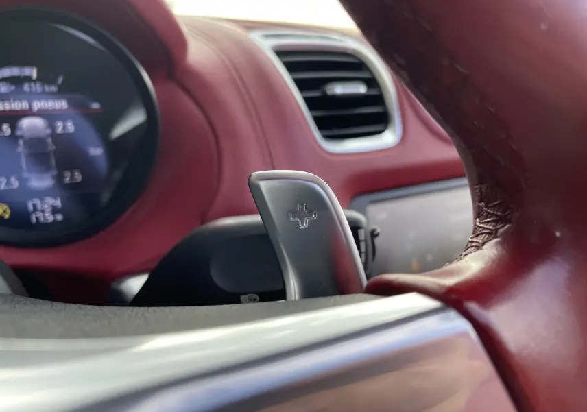 Gros plan sur la palette de changement de vitesse + du volant en cuir rouge grenat dans l'habitacle du Porsche Boxster S 2012.