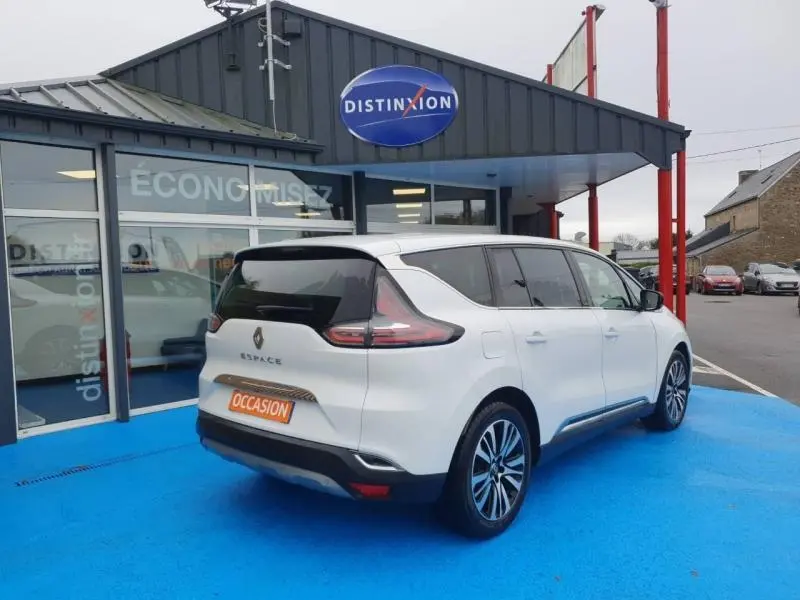 Renault Espace blanc nacré vu en 3/4 arrière droit sur parking devant concession Distinxion