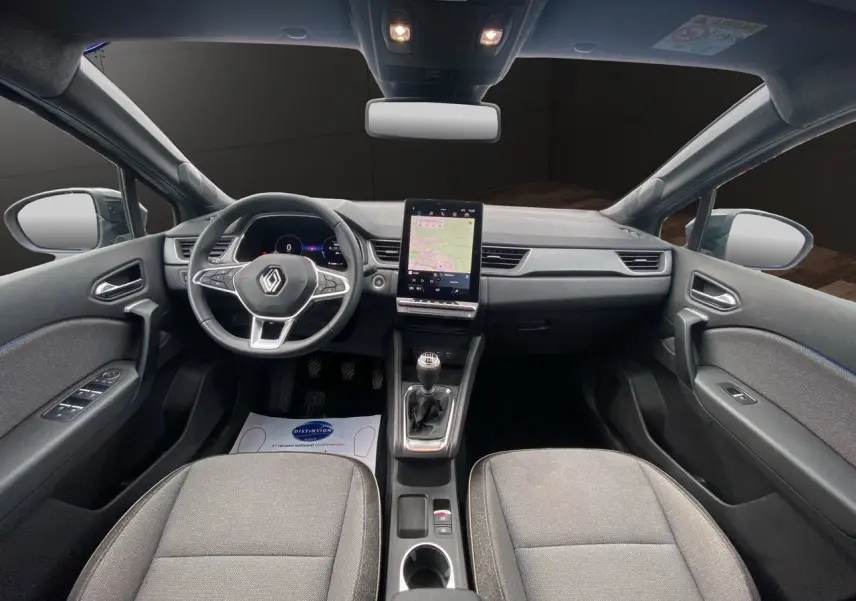 Vue intérieure avant du Renault Captur 2025 avec tableau de bord noir, écran tactile vertical et sièges tissu gris.