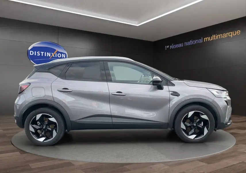Profil droit du Renault Captur 2025 gris Cassiopée avec toit noir et jantes alu 18 pouces en intérieur showroom.