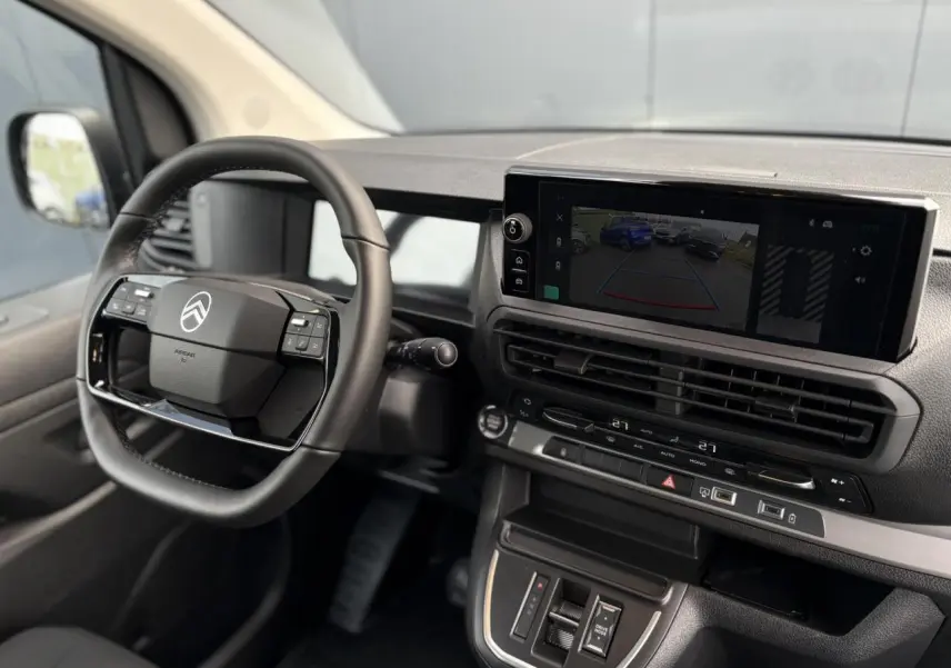 Vue intérieure côté conducteur du tableau de bord du Citroën Jumpy gris, avec écran tactile et volant cuir multifonction.