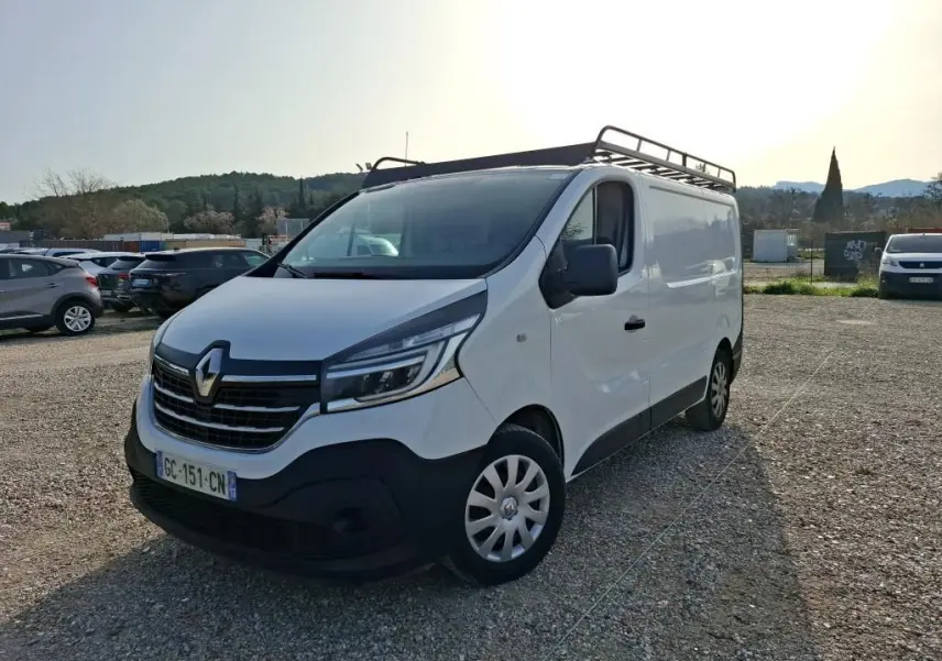 Renault Trafic Fourgon blanc vu en 3/4 avant droit avec galerie de toit et calandre noire distinctive.