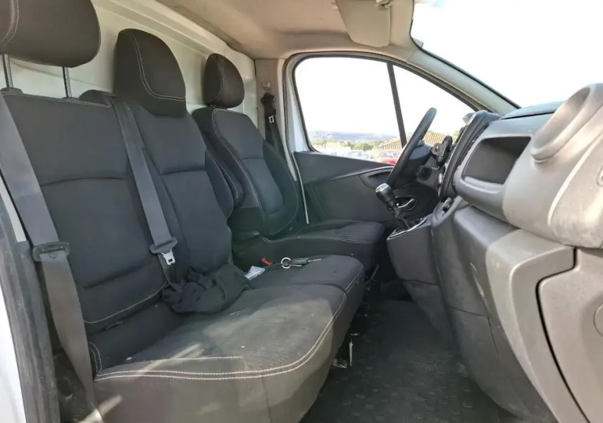 Vue intérieure côté conducteur du Renault Trafic Fourgon blanc 2021, montrant les sièges noirs et le tableau de bord.
