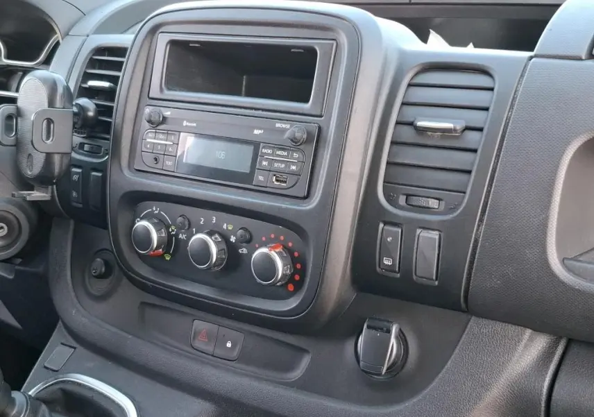 Vue rapprochée de la console centrale intérieure du Renault Trafic Fourgon blanc, avec commandes de climatisation et radio.