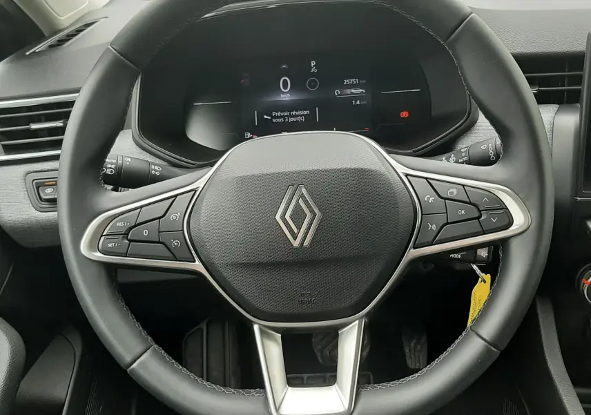 Vue intérieure centrée sur le volant noir de la Renault Clio V avec tableau de bord digital et commandes intégrées.