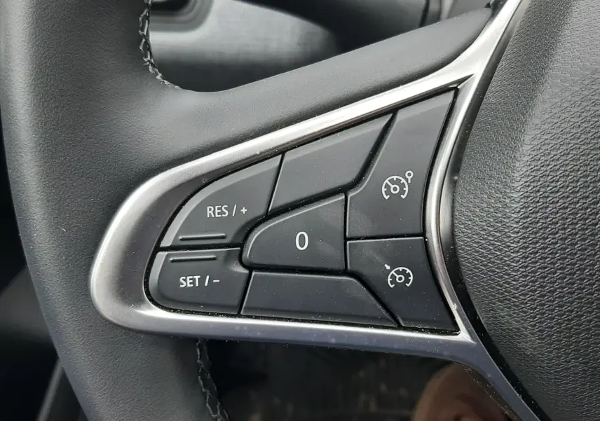 Gros plan sur les commandes de régulateur de vitesse au volant noir de la Renault Clio V gris schiste, côté gauche.