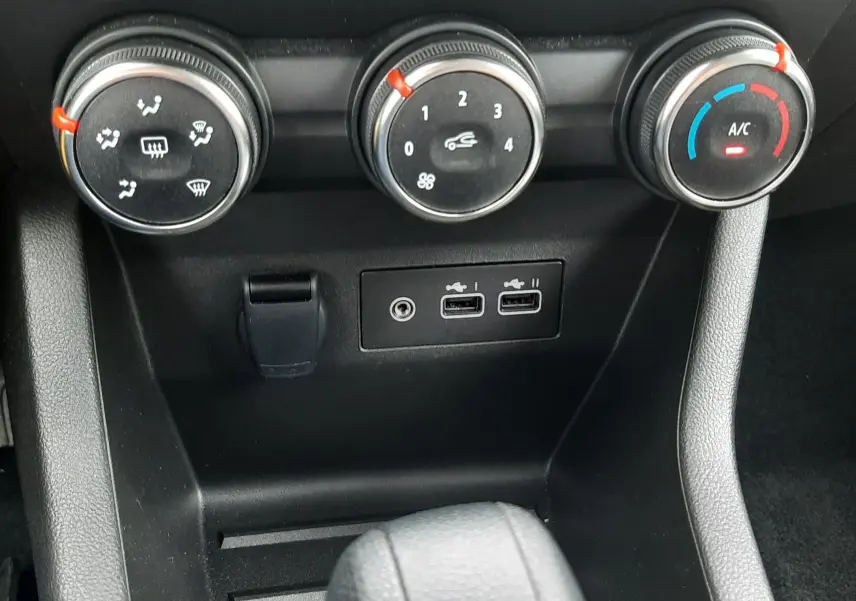 Gros plan sur les commandes de climatisation et ports USB du Renault Clio V gris schiste, version 2025, avec réglages manuels.