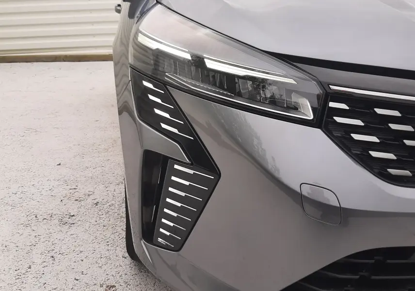 Gros plan sur l'avant droit de la Renault Clio V gris schiste, mettant en valeur ses phares LED et la calandre distinctive.