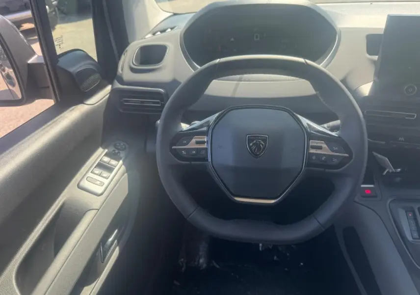 Vue intérieure centrée sur le volant cuir multifonctions du Peugeot Rifter gris avec tableau de bord et commandes côté gauche.