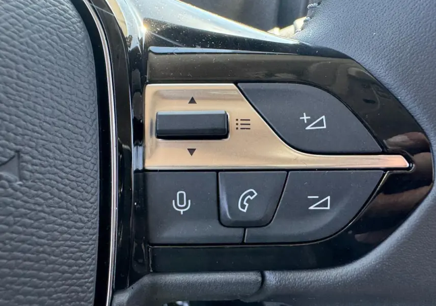 Gros plan sur les commandes multifonctions noires et dorées du volant cuir du Peugeot Rifter gris 2026.