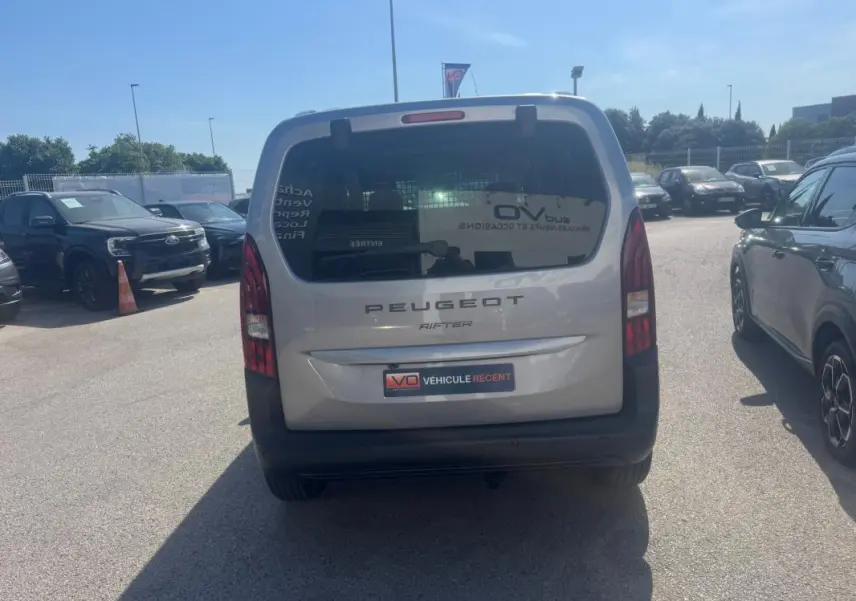 Vue arrière d'un Peugeot Rifter gris 2026 avec porte latérale et barres de toit visibles en extérieur.