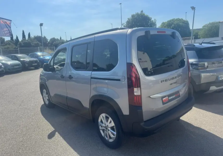 Vue 3/4 arrière droite d’un Peugeot Rifter gris 2026 avec barres de toit et jantes alliage 17 pouces.