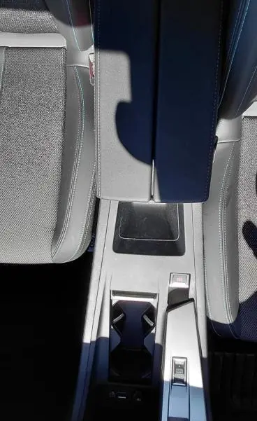 Vue plongeante sur la console centrale noire du Peugeot 408 Hybrid 145 e-DCS6 Allure avec accoudoir et porte-gobelets.