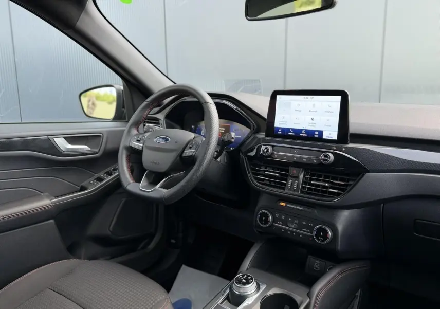 Vue intérieure côté conducteur du Ford Kuga 2023, volant ST-Line avec surpiqûres rouges et écran tactile central.
