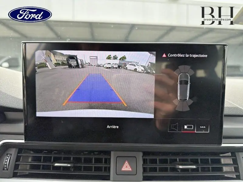Écran intérieur affichant la caméra de recul et l'aide au stationnement d'une Audi A4 Avant blanc glacier, vue de face.