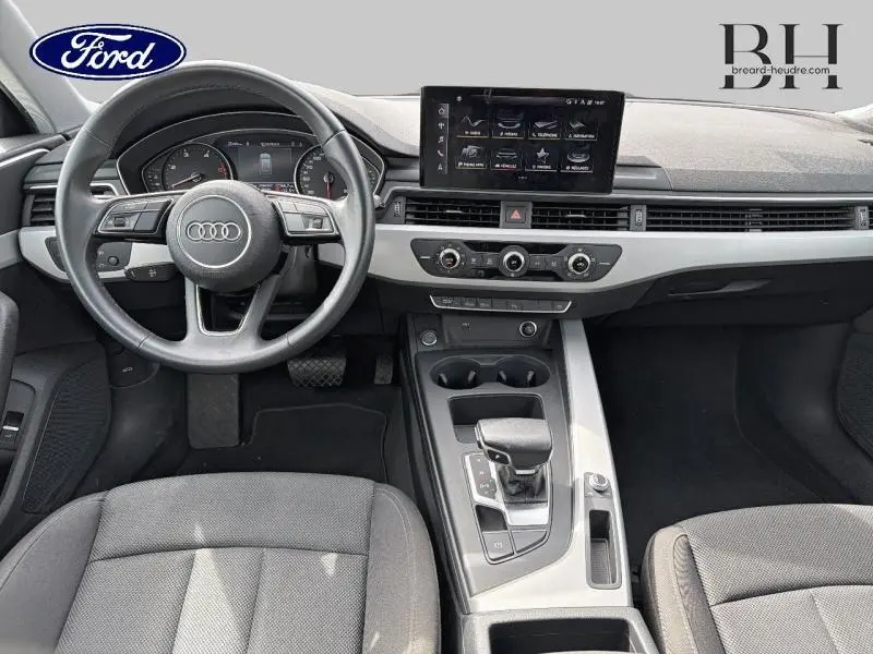Vue intérieure avant de l'Audi A4 Avant 30 TDI blanc glacier, montrant le volant, tableau de bord et console centrale.