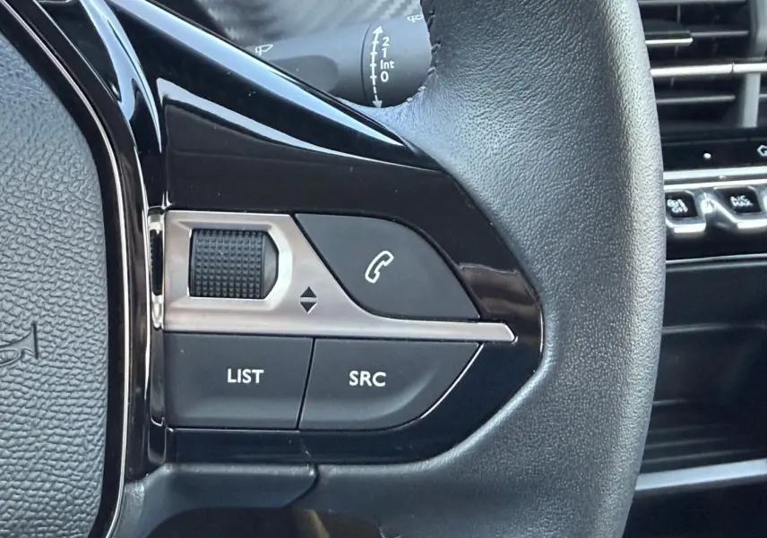 Gros plan sur les commandes audio au volant noir de la Peugeot 208 1.2 100ch Style, avec molette et boutons SRC et LIST.