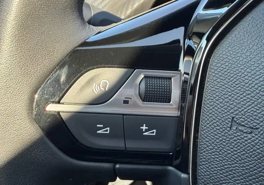 Gros plan sur les commandes vocales et volume sur le volant noir brillant de la Peugeot 208 2025.