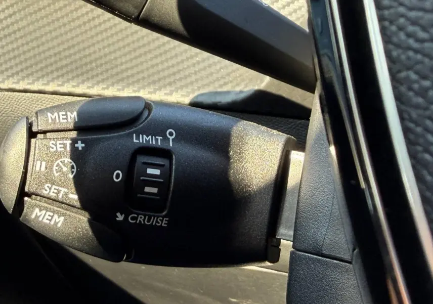 Gros plan sur la commande de régulateur de vitesse noire à gauche du volant dans l’habitacle d’une Peugeot 208 noire.