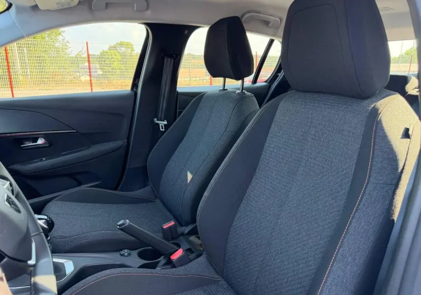 Vue intérieure côté gauche montrant les sièges avant en tissu gris avec surpiqûres orange de la Peugeot 208 2025.