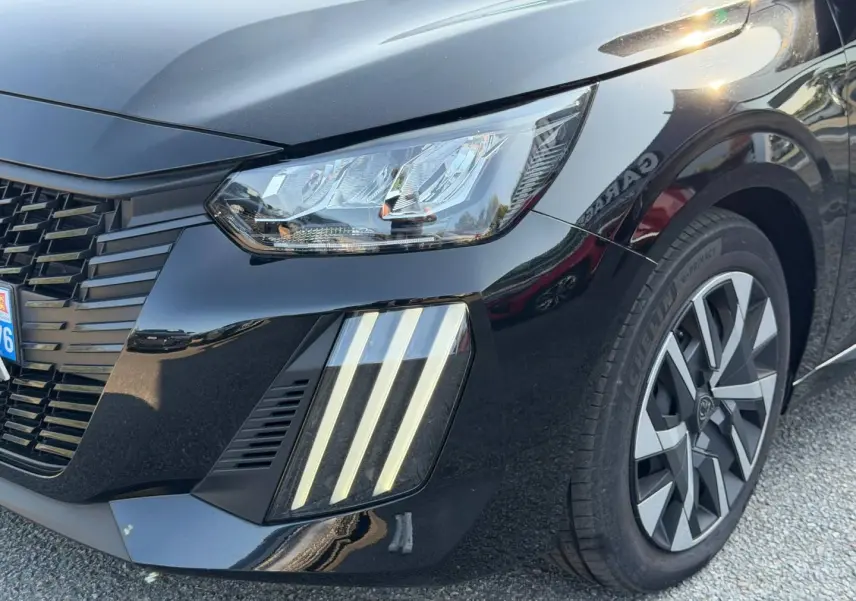 Gros plan sur l'avant droit d'une Peugeot 208 noire Perla Nera avec phares LED et jante alliage distinctive.