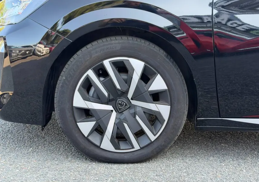 Gros plan sur la roue avant gauche de la Peugeot 208 noire Perla Nera avec jante au design géométrique moderne.