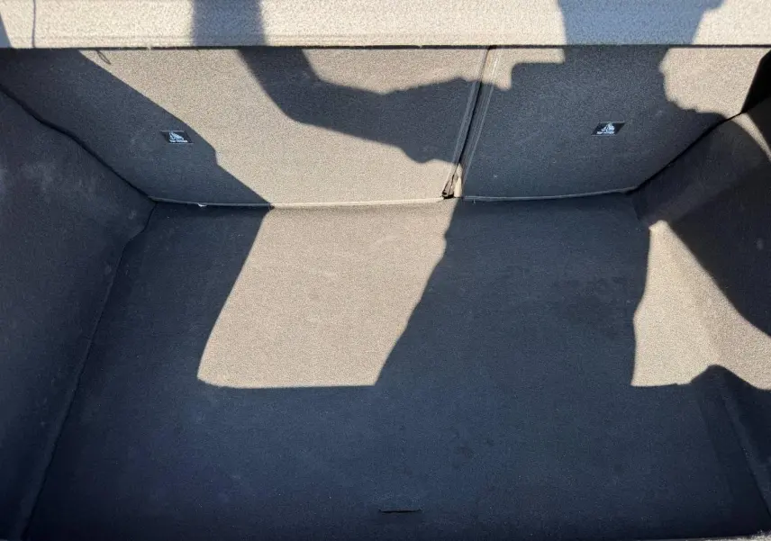 Coffre vide vu de dessus, revêtement tissu noir, banquette arrière rabattable visible en arrière-plan.