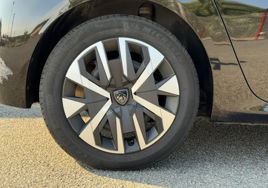Gros plan sur la roue avant gauche d'une Peugeot 208 noire Perla Nera avec jante au design géométrique bicolore.