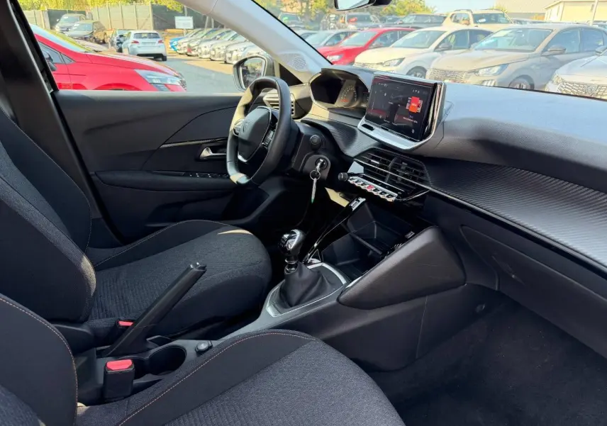 Vue intérieure côté conducteur de la Peugeot 208 1.2 100ch noire, avec tableau de bord moderne et boîte manuelle.