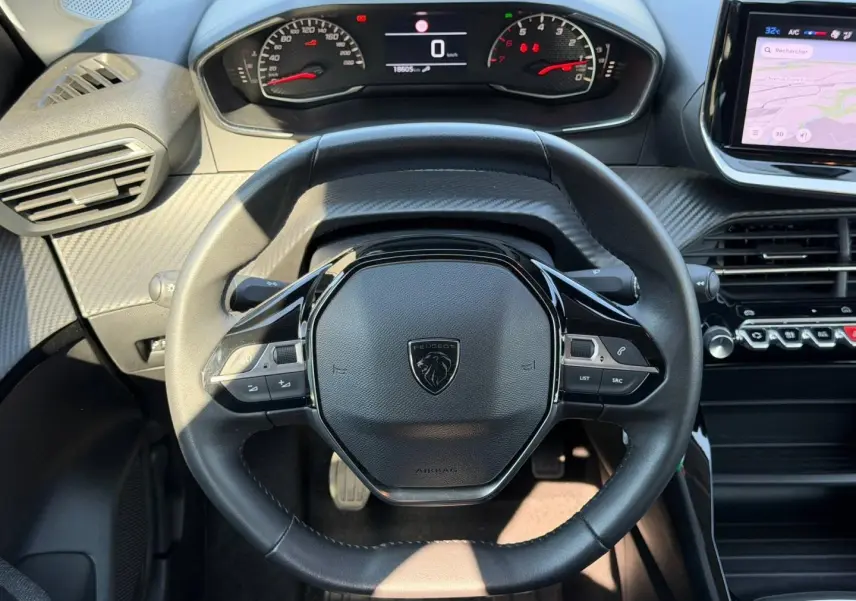 Vue rapprochée du volant noir de la Peugeot 208 1.2 100ch Style 2025, avec tableau de bord digital et écran tactile latéral.