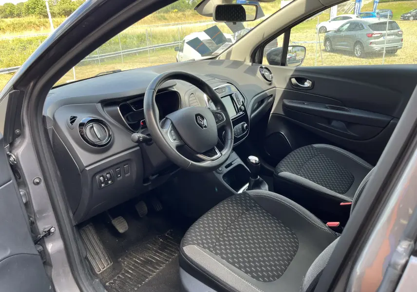Intérieur avant gauche du Renault Captur gris 2019, volant cuir, tableau de bord avec écran tactile et sièges tissu noirs.