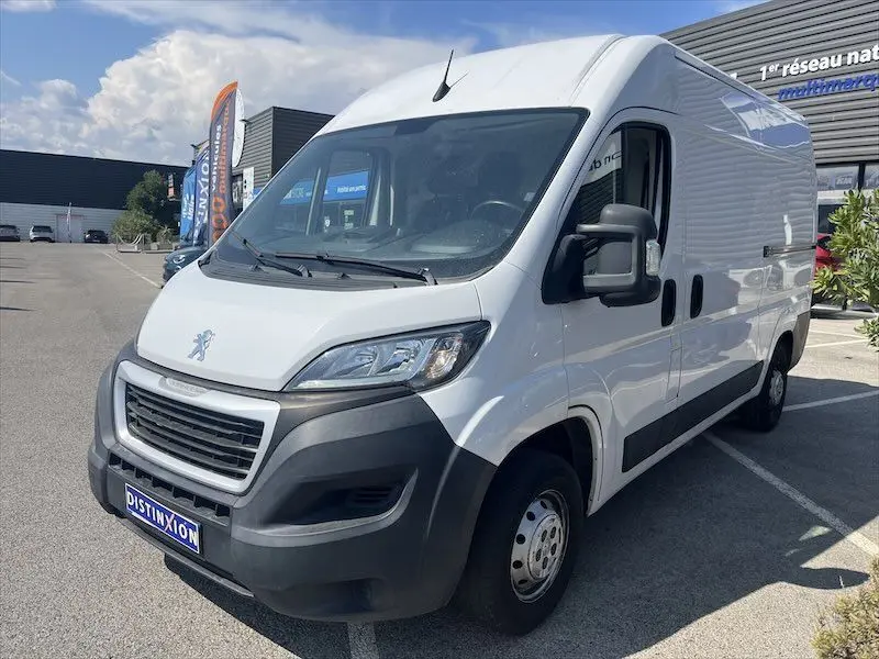 Vue 3/4 avant droit d’un utilitaire Peugeot Boxer blanc avec deux portes latérales, stationné en extérieur.