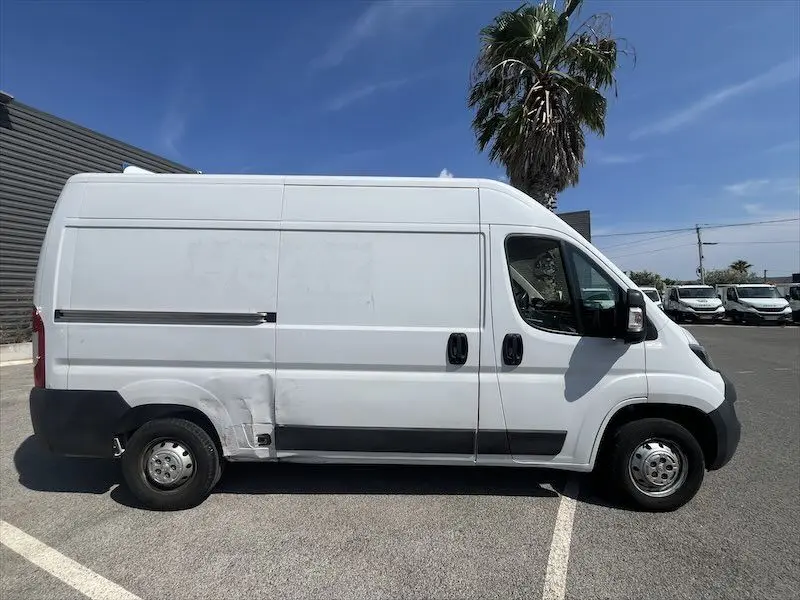 Profil côté droit d'un utilitaire Peugeot Boxer blanc avec deux portes latérales, stationné en extérieur sous un ciel bleu.