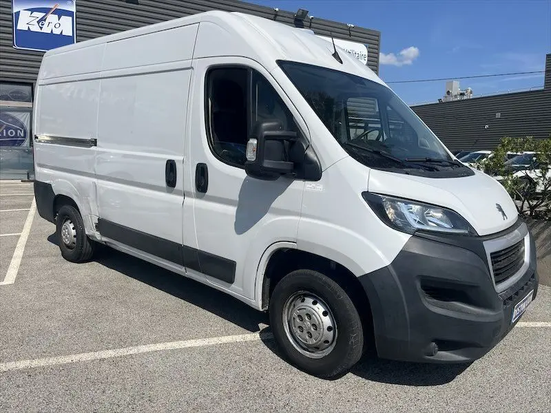 Vue 3/4 avant droite d’un utilitaire Peugeot Boxer blanc avec deux portes latérales, stationné en extérieur.