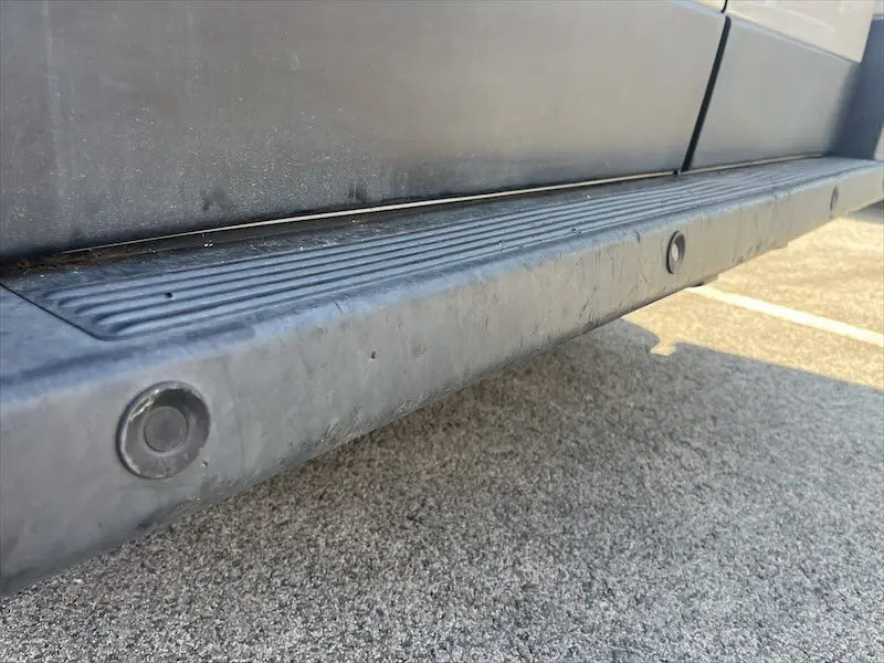 Gros plan sur la marche latérale noire du côté droit du Peugeot Boxer FGN blanc, visible sur un sol goudronné.