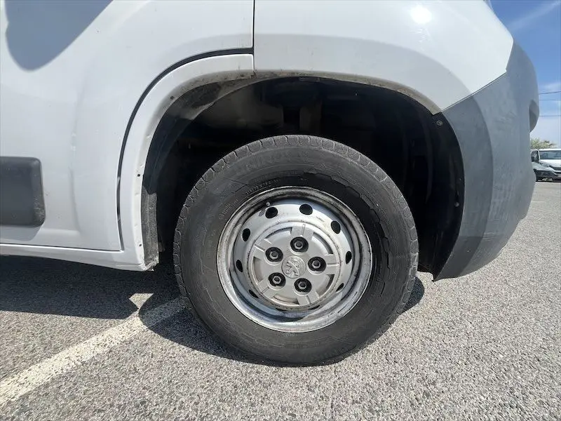 Gros plan sur la roue avant gauche d'un Peugeot Boxer blanc, avec jante acier et logo Peugeot visible au centre.