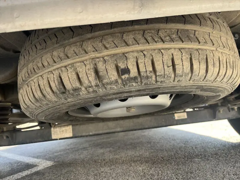 Gros plan sous le Peugeot Boxer FGN 2021 sur la roue de secours montée sous le châssis, pneu usé et jante acier grise.