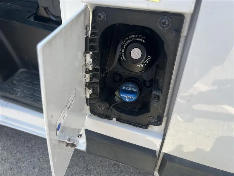 Gros plan sur la trappe de carburant ouverte côté droit du Peugeot Boxer blanc, montrant les bouchons Diesel et AdBlue.
