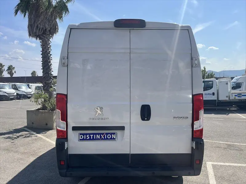 Vue arrière d'un Peugeot Boxer blanc avec portes battantes et logo Distinxion sur parking ensoleillé.