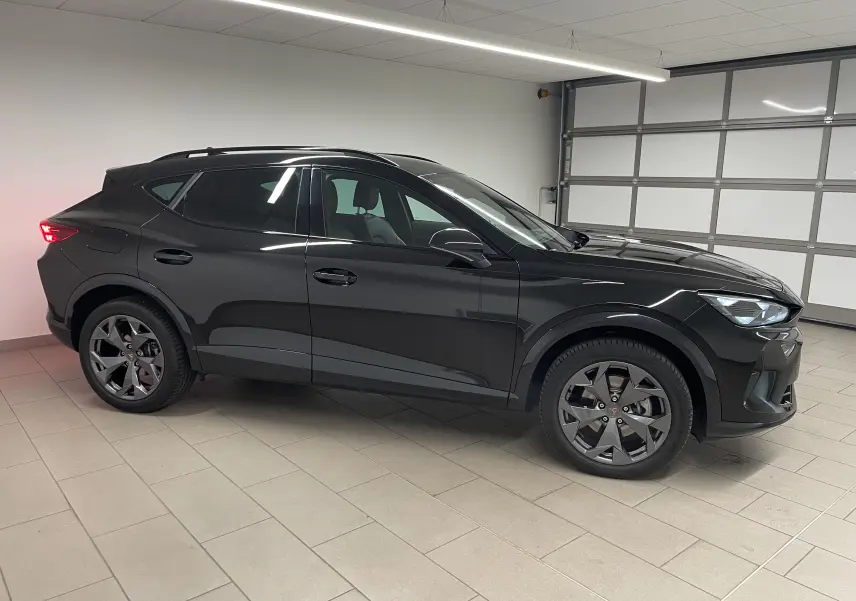 Vue de profil côté gauche d'un CUPRA Formentor 2025 noir minuit avec jantes foncées dans un garage intérieur.