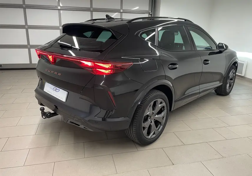 Vue 3/4 arrière droite du CUPRA Formentor noir minuit avec feux allumés et crochet d'attelage escamotable visible.