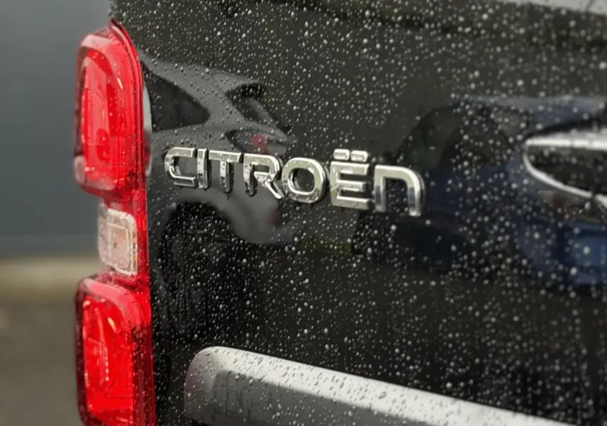 Gros plan sur l'arrière gauche noir perla d'un Citroën Jumpy avec logo et feux rouges sous la pluie.