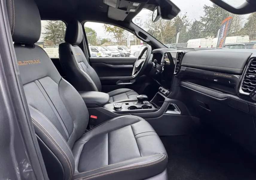 Vue intérieure côté conducteur du Ford Ranger Wildtrak 2025, sièges noirs avec surpiqûres orange et tableau de bord moderne.