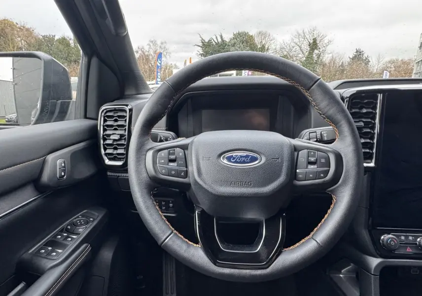 Vue intérieure centrée sur le volant cuir noir avec surpiqûres marron du Ford Ranger 2025, tableau de bord et écran tactile visibles.