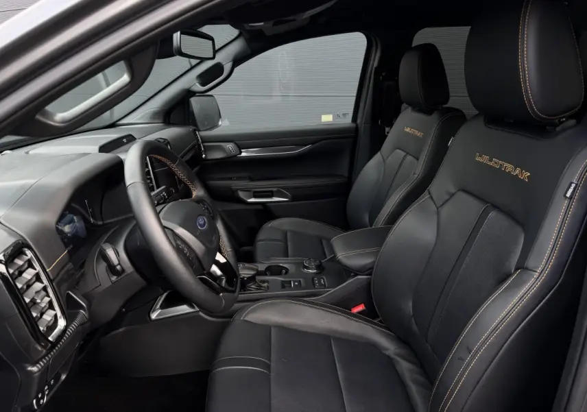 Vue intérieure côté conducteur du Ford Ranger Wildtrak 2025, sièges noirs avec surpiqûres orange et logo Wildtrak brodé.