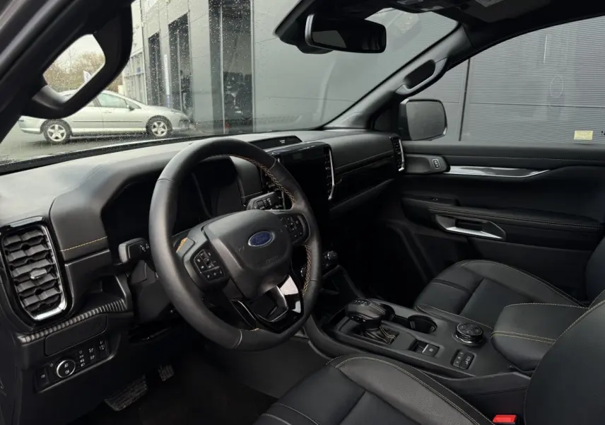 Vue intérieure côté conducteur du Ford Ranger 2025, tableau de bord noir avec coutures jaunes et écran tactile central.