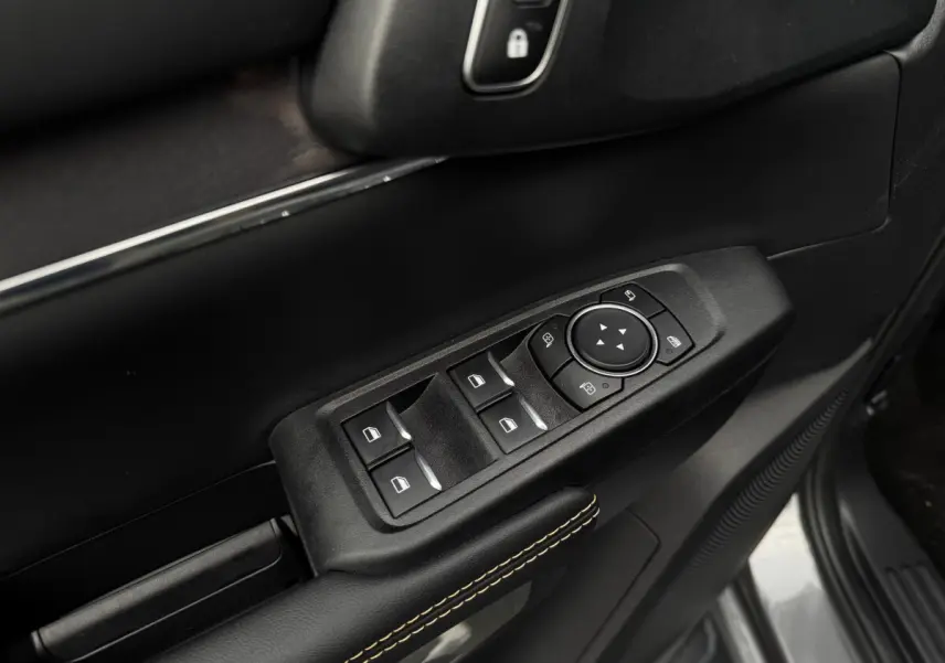 Gros plan sur la commande des vitres et rétroviseurs côté conducteur, garniture noire avec surpiqûres jaunes.