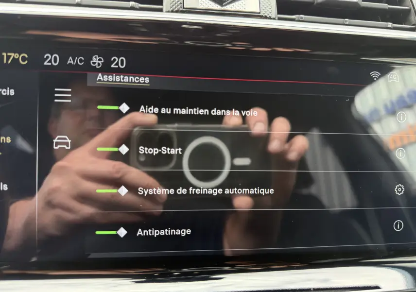 Écran tactile intérieur du DS7 2025 affichant les assistances à la conduite, avec reflet des mains et du smartphone.